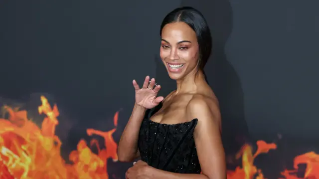 Zoe Saldaña at the European premiere of Avatar: Fire and Ash in France against a backdrop covered in flames