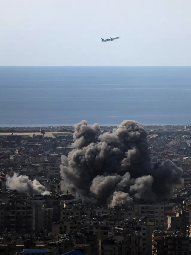 An airplane flies as smoke rises after an Israeli strike on Beirut's southern suburbs