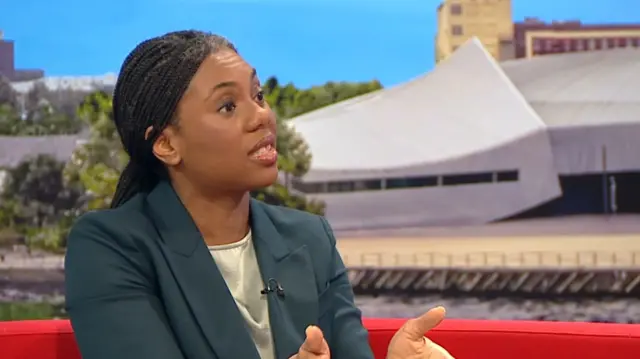 Kemi Badenoch in a teal blazer speaking to BBC Breakfast on the red sofa with her hands out gesticulating