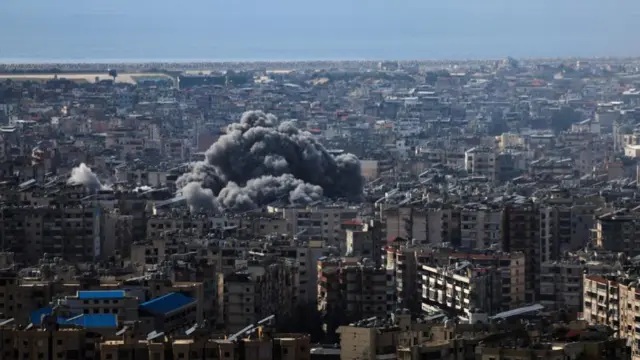 A thick grey smoke plume mushrooms over a dense urban area