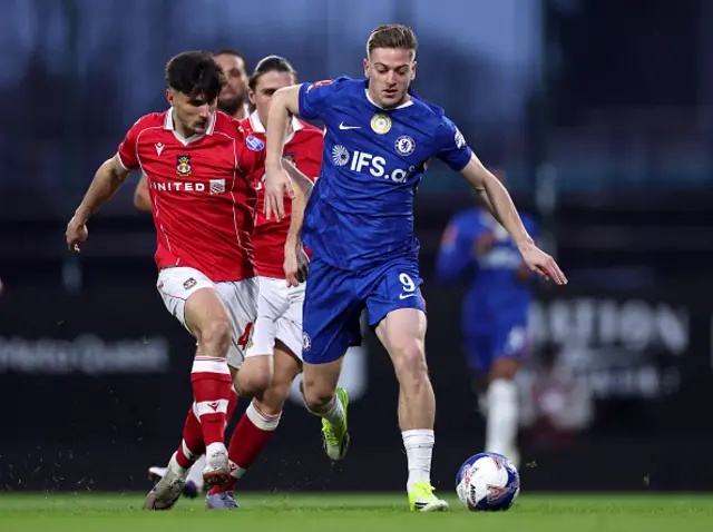 Liam Delap of Chelsea runs with the ball whilst under pressure from Ryan Longman