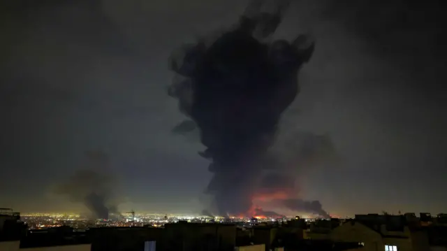A tall, wide and dark plume of smoke rises from the site of strikes at Mehrabad International Airport.