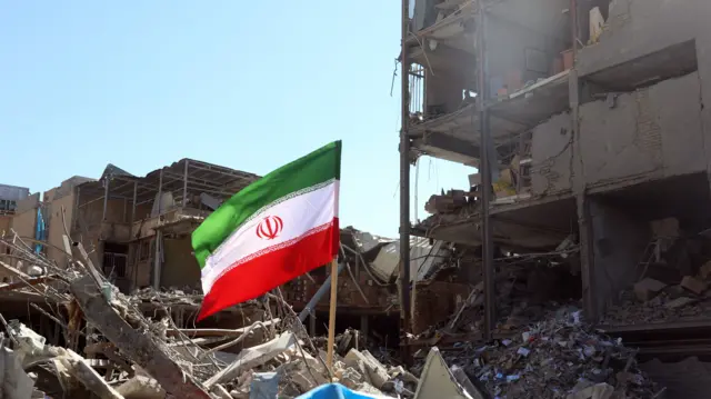An Islamic Republic of Iran flag on a pole in the middle of debris of a destroyed home in the centre of Tehran