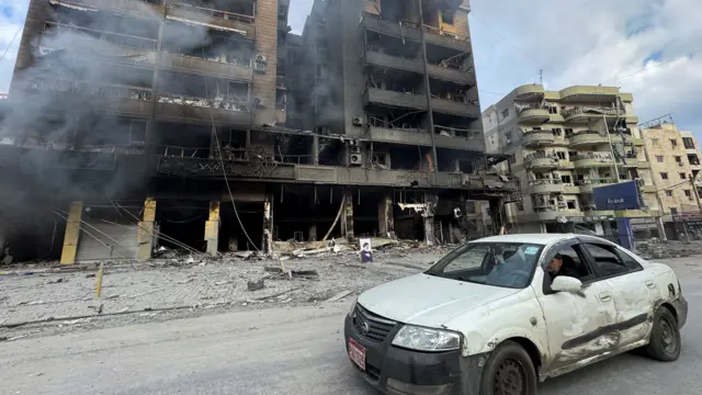 A car drives past burned buildings after an Israeli strike on Beirut's southern suburbs