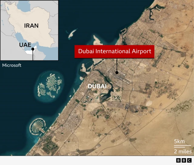 A satellite map of Dubai showing the location of Dubai International Airport marked with a red label. The map includes major landmarks such as Palm Jumeirah and The World islands along the coast. An inset map in the top-left corner shows the UAE’s position relative to Iran. A scale bar indicates distances of 5 km and 2 miles. There are BBC blocks in the bottom-right corner.