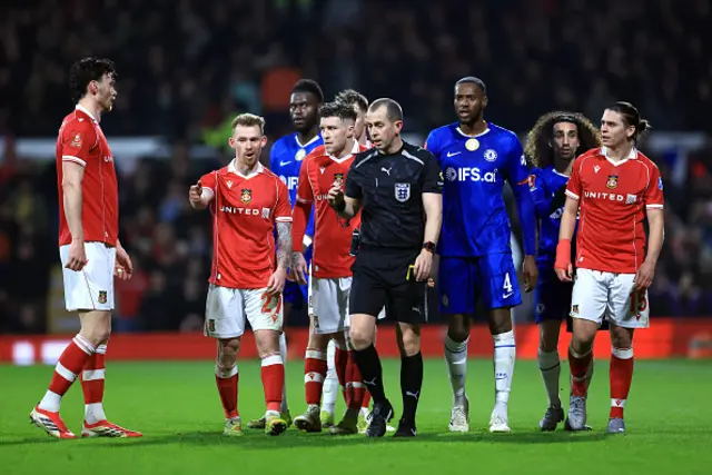 Lewis O'Brien of Wrexham speaks to Referee Peter Bankes as a VAR review takes place before a red card is awarded to George Dobson