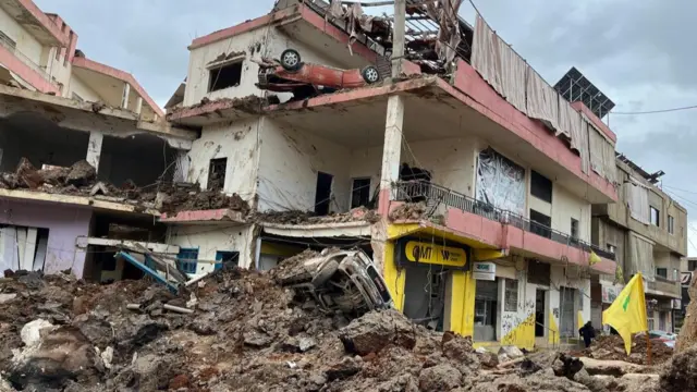 Damage from strikes in the village of Nabi Chit in the Bekaa Valley in eastern Lebanon. A partially-destroyed building and destroyed cars are visible alongside rubble.