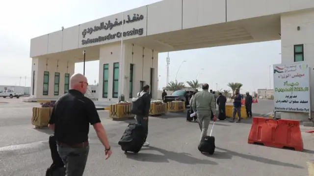 People wheel suitcases across a border point