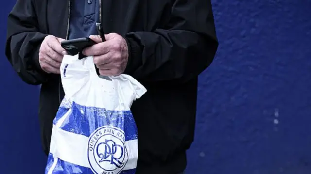 A QPR fan checks his phone outside Loftus Road