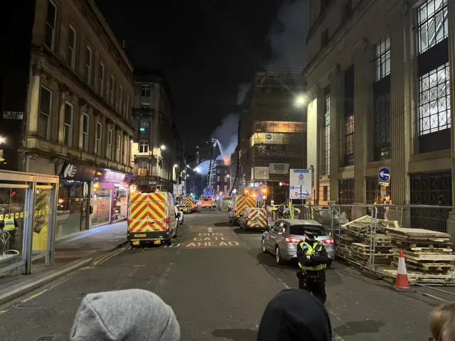 Street view at night in Glasgow city centre. Emergency vehicles are parked up and firefighters can be seen tackling the blaze from a height
