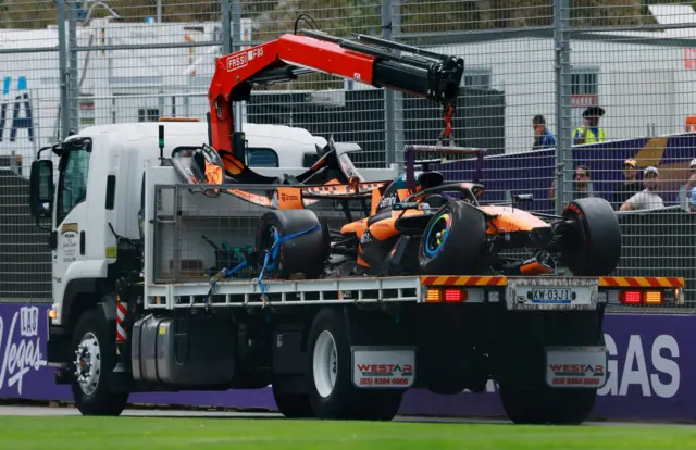 The damaged McLaren of Oscar Piastri is driven away on a track after he crashed on his way to the grid