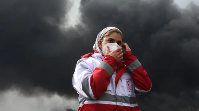 A woman in a white and red uniform clutches a face mask to her mouth
