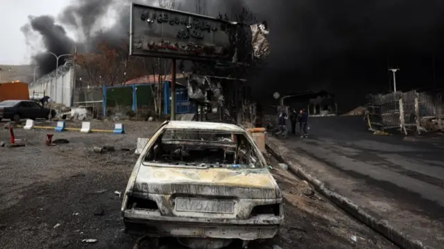 A charred car in front of a gutted building in the aftermath of a strike