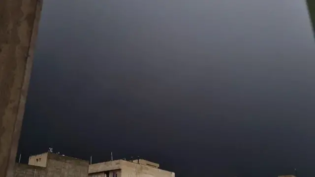 A photo showing the sky blanketed in grey with some rooftops in the bottom left corner.