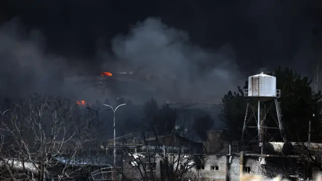 A smoky landscape with two small fires visible in the foreground