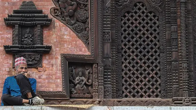 An old Nepali man stis in front of a temple in Kathmandu