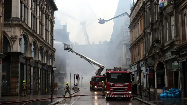 Three aerial ladders dampen down at the scene. There are fire engines and firefighters at the scene.