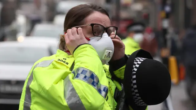 Police officer adjusting a mask on her face.