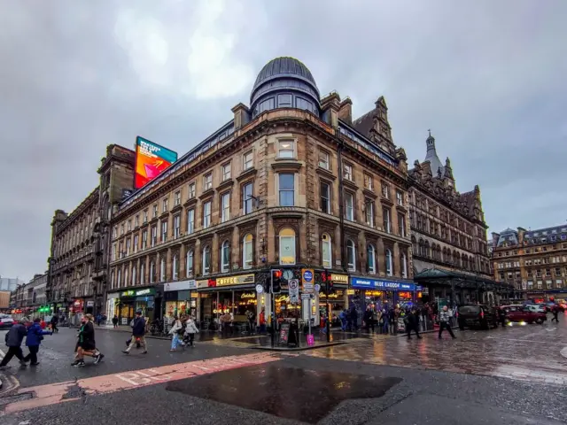 Building at the corner of Union Street and Gordon Street on a grey day in Glasgow. There are lots of people on the street.