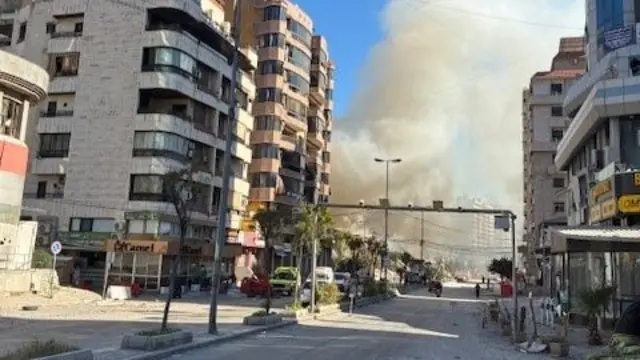 A street scene in Lebanon. About halfway down the street a building has been hit by an apparent strike and smoke is billowing out