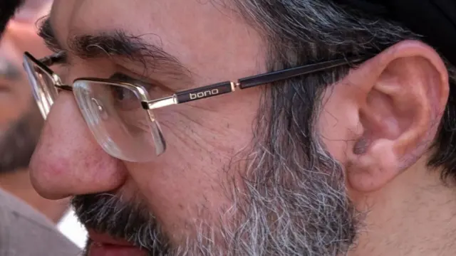 A close up shot shows Mojtaba Khamenei with glasses and a beard