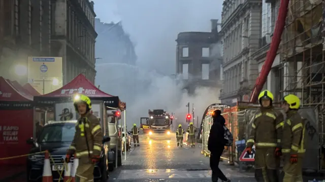 Firefighters with the burnt-out building behind them
