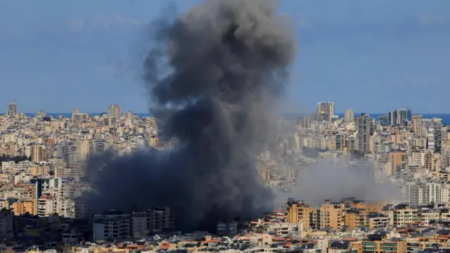 A large plume of smoke rising from an area packed with building