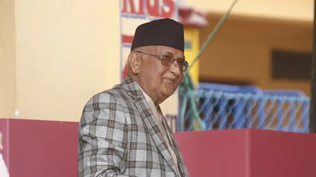 K P Sharma Oli wears a checked grey jacket and glasses
