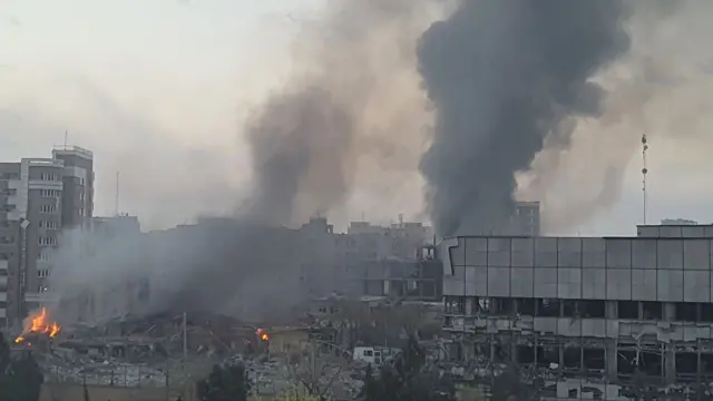 Large smoke plumes next to a partially destroyed building