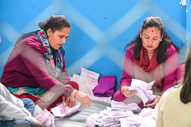 Two women sitting on the floor counting ballots cast during the Nepal 2026 election