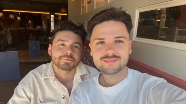 Two men with short, brown hair and beards smile for a selfie