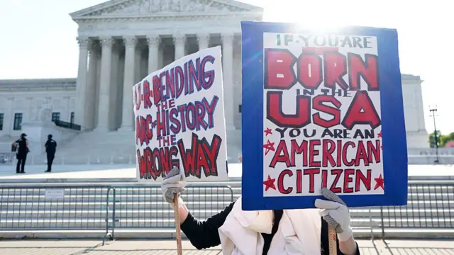 A woman stands outside the Supreme Court holding two signs protesting Trump's executive order