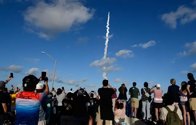 Crowd points phones to the sky as they take pictures of rocket take off