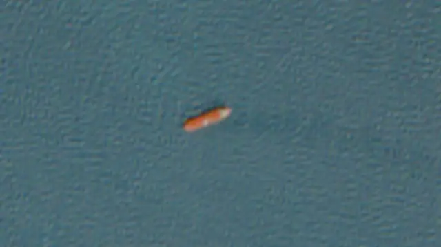 A satellite image showing an orange ship in the sea