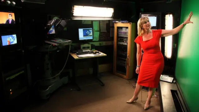Carol Kirkwood stands in front of a green screen in a red dress