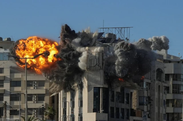 An explosion goes off following a missile strike on a high building in Beirut. Large clouds of grey and black smoke emerge from inside the building as a fireball extends to the left side of the property