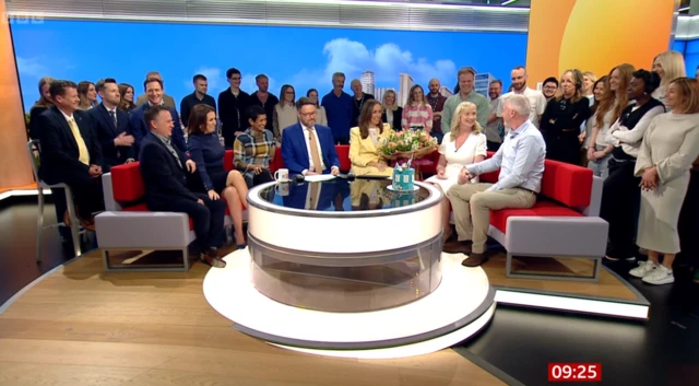 Carol Kirkwood surrounding by group of people at BBC Breakfast studio.