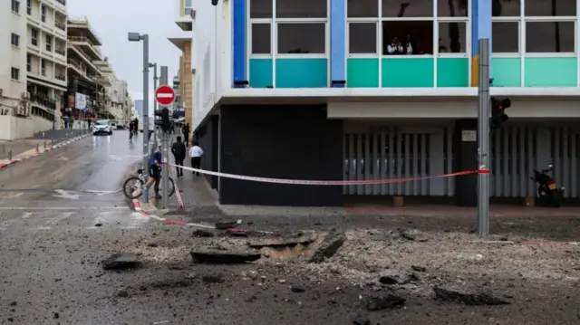 Debris on the streets of Tel Aviv outside a residential building, another street with people walking away on the left