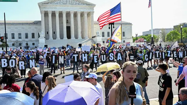Толпы протестующих держат табличку с надписью «Рожденный в США = гражданин».