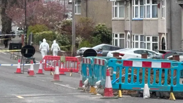 Forensics officers are walking down a road by a crime scene.