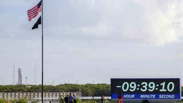 The rocket in the far distance with a big clock on a green counting down time until launch. A flag pole bears the American flag