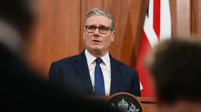 Keir Starmer wears a dark suit and tie while delivering a press conference at Downing Street.