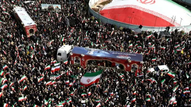 Thousands of people attend a funeral ceremony in Tehran for Islamic Revolutionary Guard Corps naval commander Alireza Tangsiri. Many hold Iranian flags.