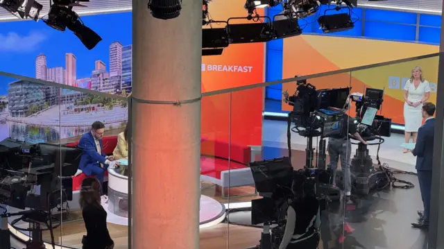 A wide view from above the BBC Breakfast studio showing Carol in the corner being filmed by a big TV camera as she presents