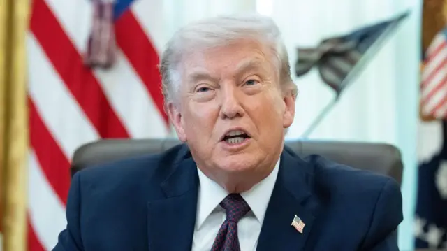 A file photo of Trump seated in the Oval Office addressing others in the room from behind his desk