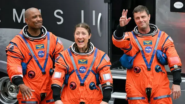 Astronauts Victor Glover, Christina Koch and Reid Wiseman smile and wave