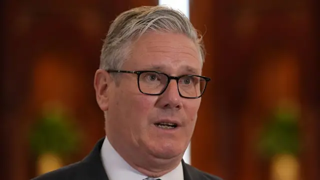 स्टार्मर के बोलने का हेडशॉट। पृष्ठभूमि धुंधली और लाल है