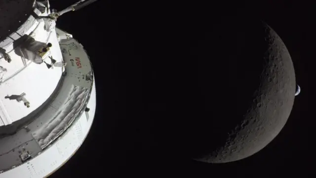 The right side of Nasa’s Orion spacecraft is seen lit up by the Sun while a waxing crescent Moon is visible behind it alongside a small crescent Earth