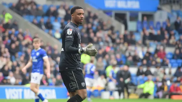 A photo of Nathan Trott playing for Cardiff City in a black goalkeeping kit with yellow and black striped goalkeeping gloves