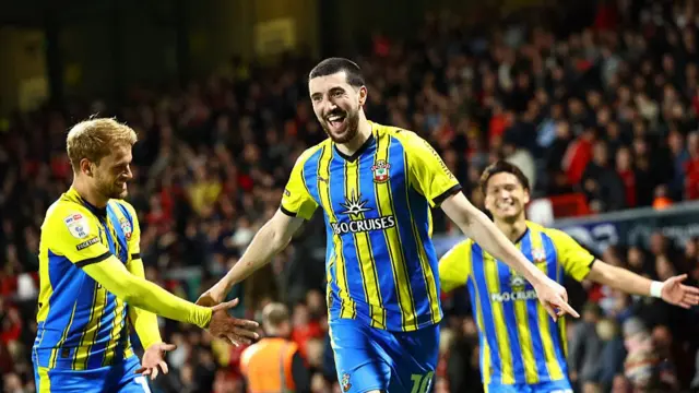 Finn Azaz of Southampton celebrates with his arms outstretched at his sides, wearing Southampton's blue and yellow striped away kit